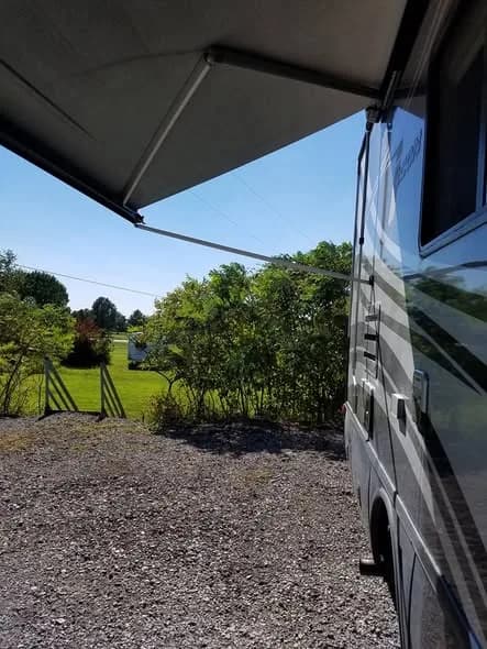 The view from under an RV awning across the green field and treeline